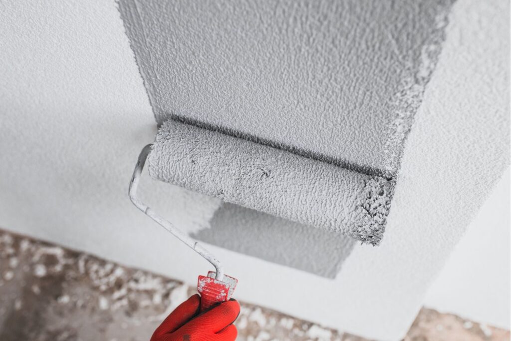 Paint Roller Being Used To Paint Gray Onto A White Wall.